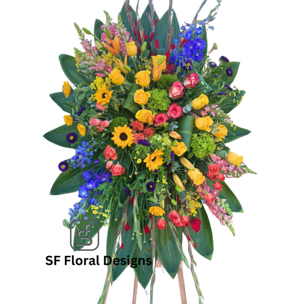 Tall multicolor standing spray with roses, lilies, delphinium, gerbera daisies, and snapdragons on a wooden easel.