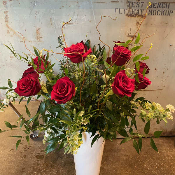 Red roses arranged in a white vase with greenery