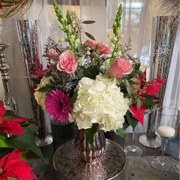 Mixed floral arrangement with pink roses, white hydrangea, and red poinsettias in a vase