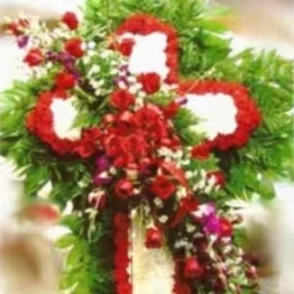 Standing funeral cross of red and white flowers with cascading red blooms on a green foliage base.