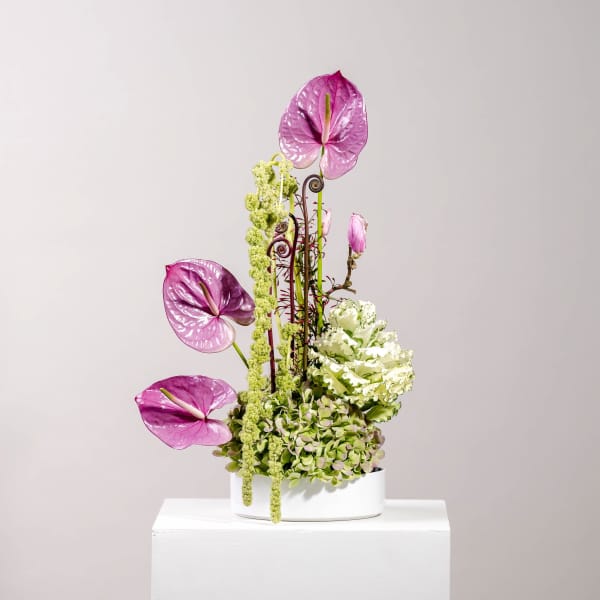 Tall floral arrangement with pink anthuriums and green blooms in a white container