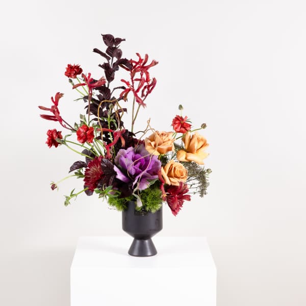 Tall floral arrangement in a black pedestal vase with red, purple, and peach blooms