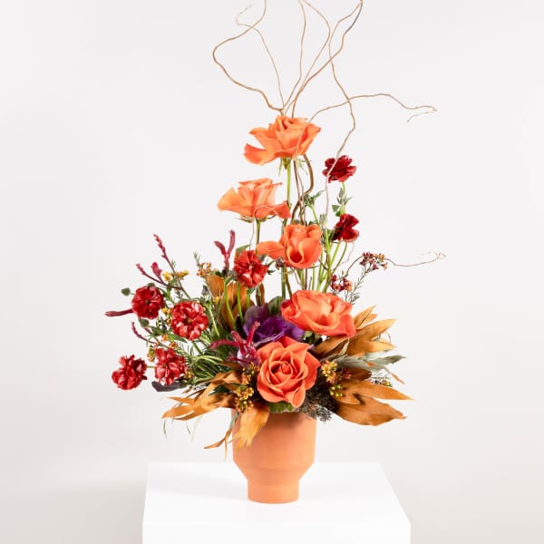 Orange and red floral arrangement in a terracotta vase with tall branches