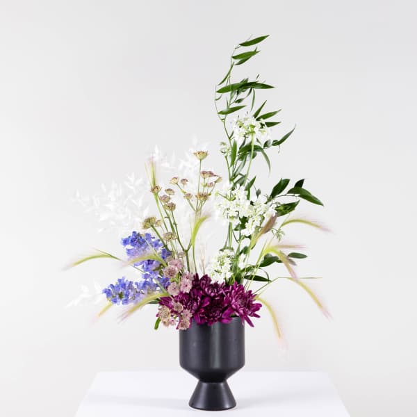 Tall floral arrangement in a black vase with purple, white, and blue blooms