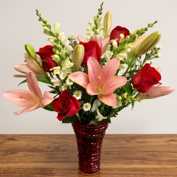 Red roses and pink lilies arranged in a red glass vase
