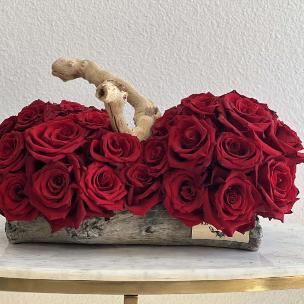 Red roses arranged in a rustic wooden container with a branch accent