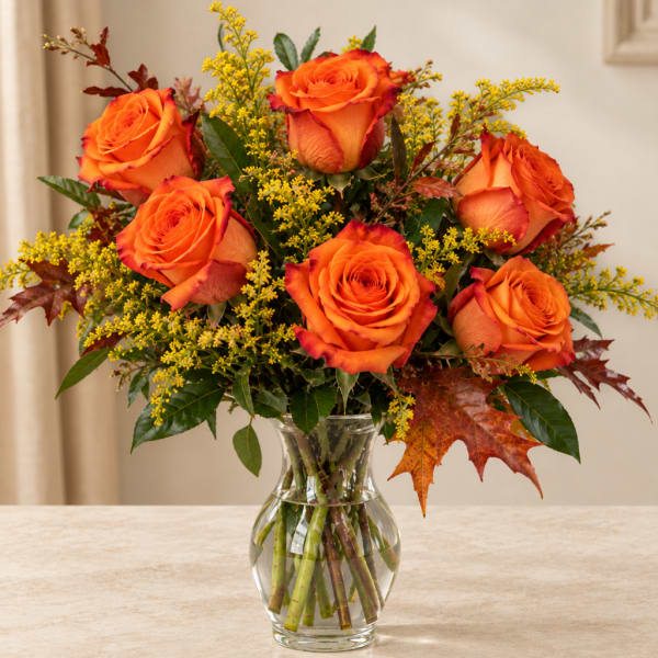 Orange roses in a clear glass vase with yellow filler flowers
