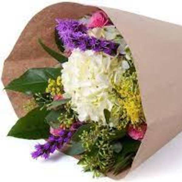 Hand-tied bouquet of white hydrangea with purple, yellow, and pink blooms wrapped in brown kraft paper.