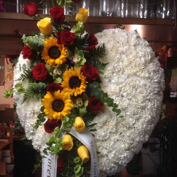 Large heart-shaped floral spray with white flowers, red and yellow roses, and sunflowers