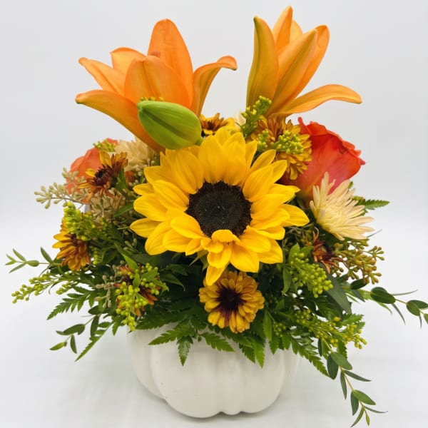 Orange lilies and a yellow sunflower arrangement in a white pumpkin vase