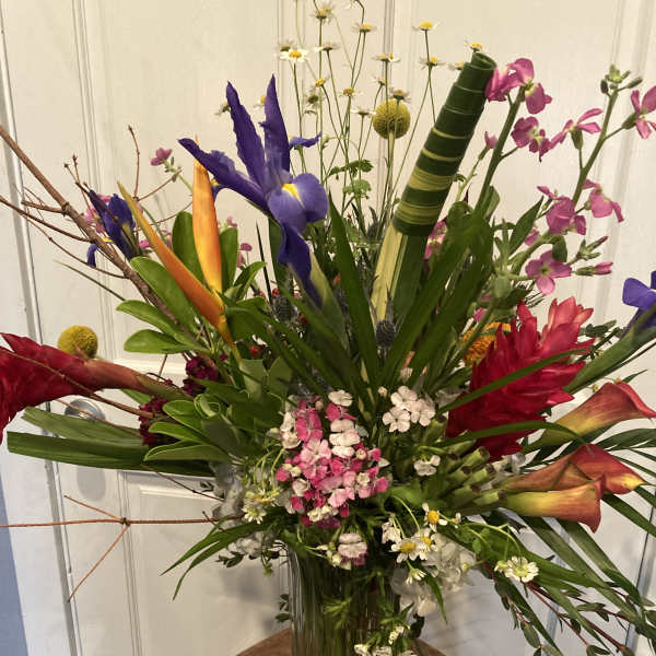Tropical flower arrangement in a clear glass vase with purple iris and pink blooms