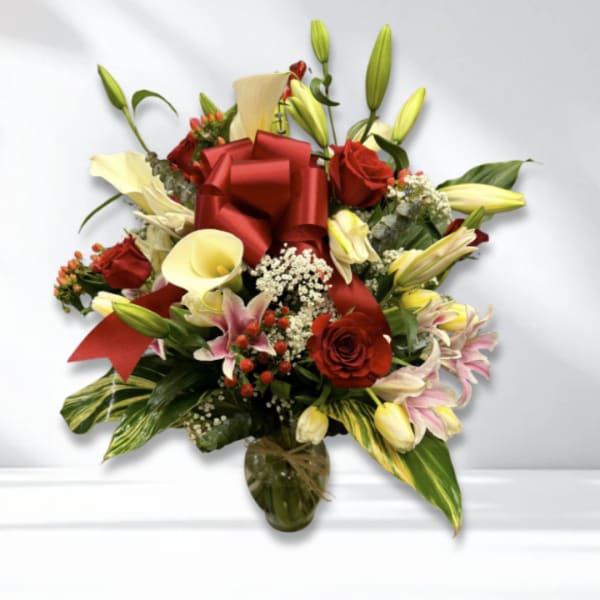 Red roses and cream lilies arranged in a glass vase with a red bow