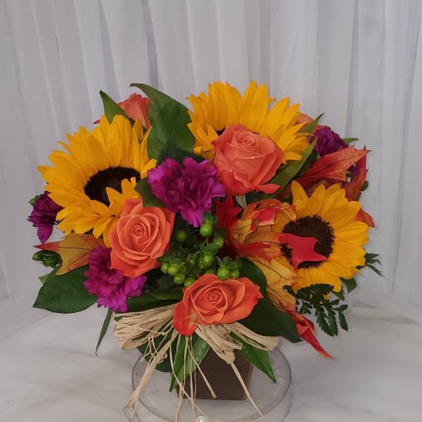 Bouquet of sunflowers, coral roses, and purple carnations in a low container