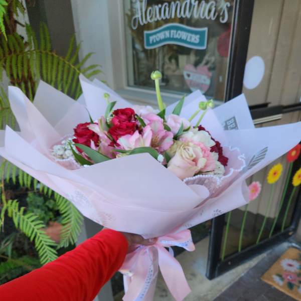 Handheld bouquet of pink and red flowers wrapped in pale pink paper