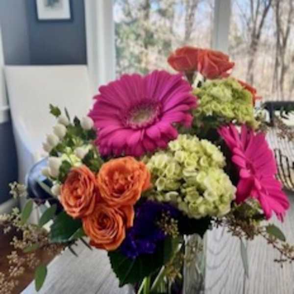 Colorful bouquet in a clear square vase with pink daisies and orange roses
