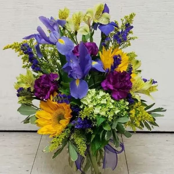 Mixed bouquet with purple, yellow, and blue flowers in a glass vase