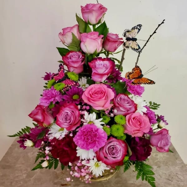 Tiered pink rose arrangement with butterfly picks in a low basket