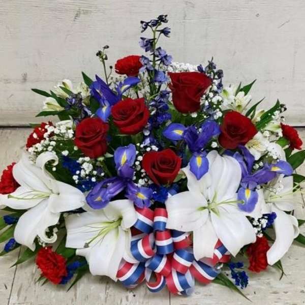 Patriotic red, white, and blue floral arrangement with roses, lilies, and ribbon bow