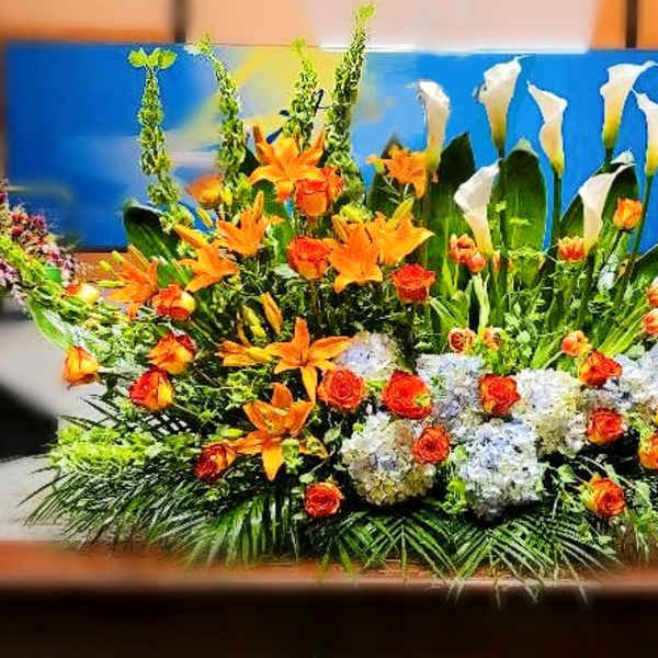 Large altar-style arrangement with orange lilies and roses, white calla lilies, and white hydrangeas