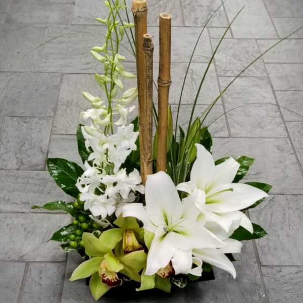 Modern arrangement of white lilies and orchids with bamboo in a low black container