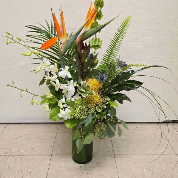 Tall tropical arrangement with orange bird-of-paradise and white orchids in a glass vase