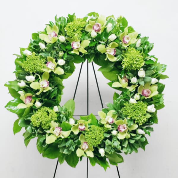 Green floral wreath with orchids and roses displayed on a black metal easel