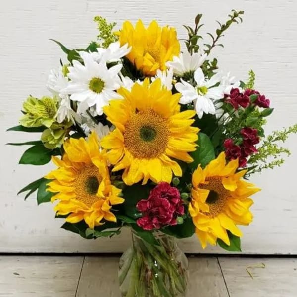 Bouquet of sunflowers, white daisies, and red flowers in a glass vase