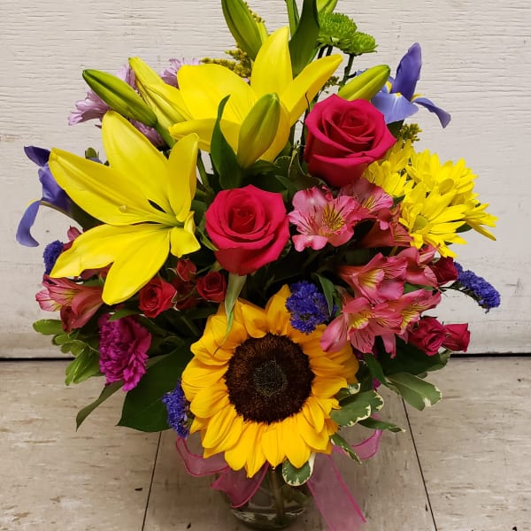 Mixed bouquet with yellow lilies, pink roses, and a sunflower in a glass vase