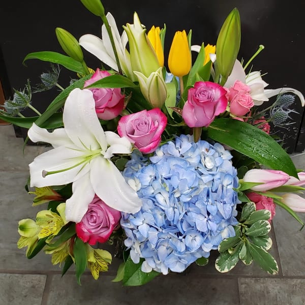Bright mixed arrangement with pink roses, white lilies, yellow tulips, and blue hydrangea