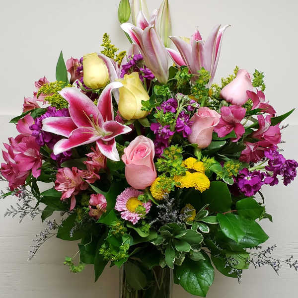 Mixed bouquet of pink lilies, roses, and yellow blooms in a glass vase
