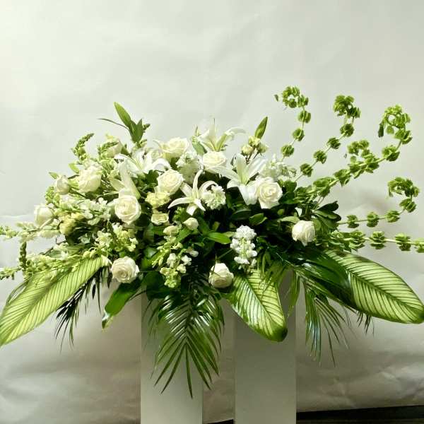 White floral arrangement with roses and lilies in a tall white pedestal vase
