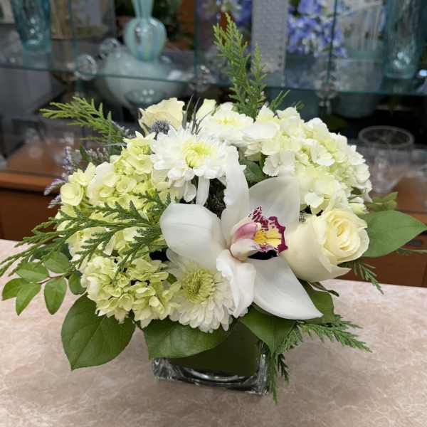 White and pale green floral arrangement in a square glass vase