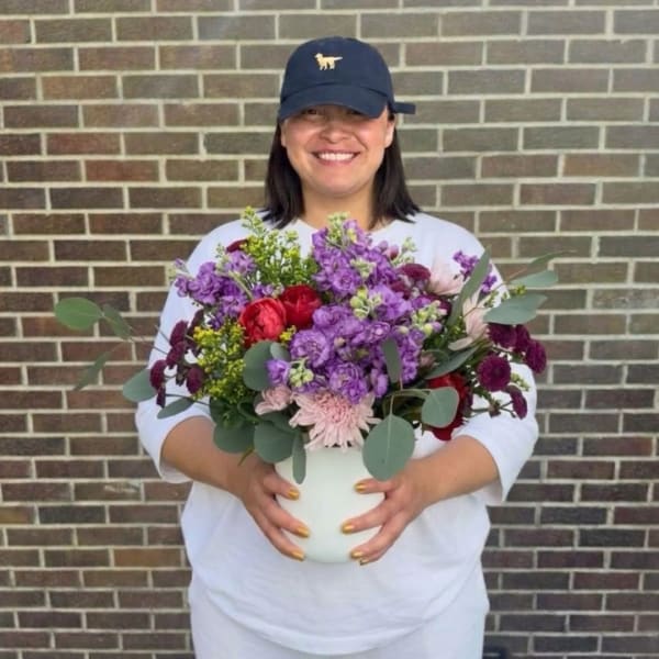 Woman holding a white vase of purple and red flowers
