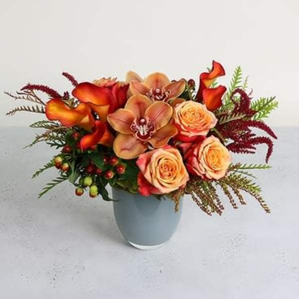 Orange calla lilies and peach roses in a light blue vase