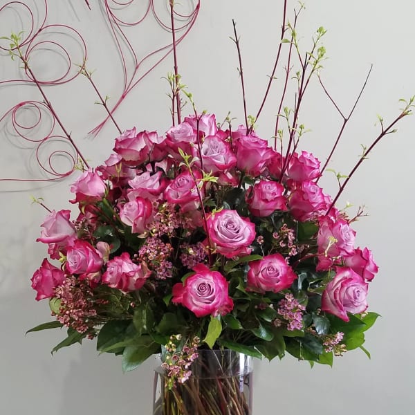 Tall arrangement of pink roses with flowering branches in a clear glass vase on a wooden table