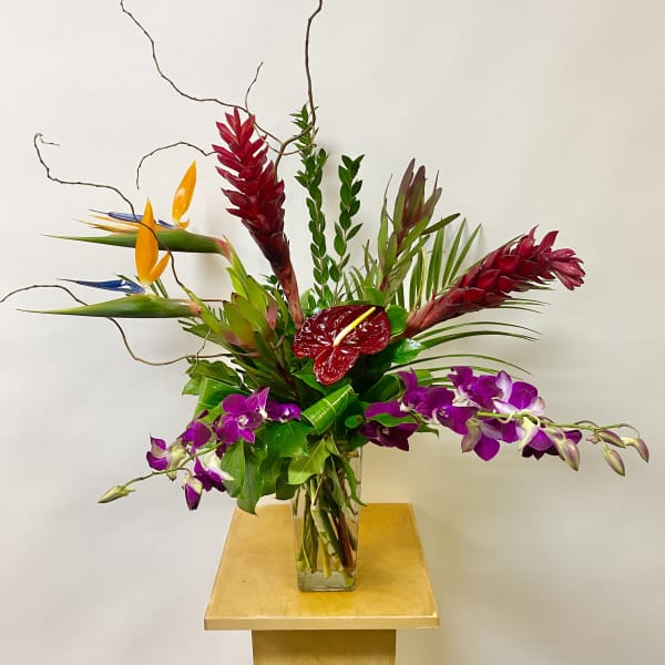 Tropical floral arrangement in a glass vase with purple orchids and red anthurium