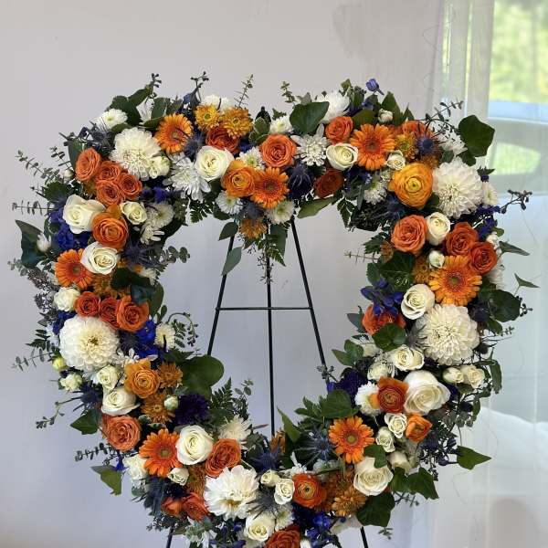 Heart-shaped floral wreath with orange, white, and blue flowers on a stand