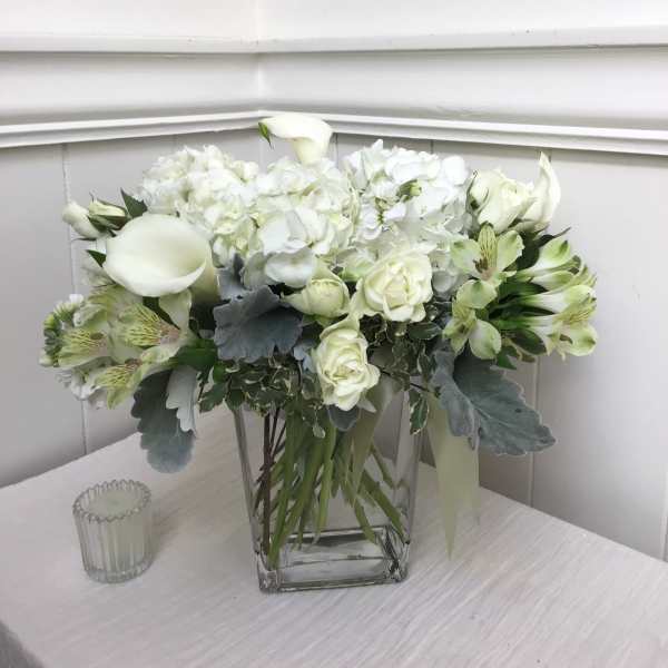 White floral arrangement in a clear square vase with calla lilies and roses