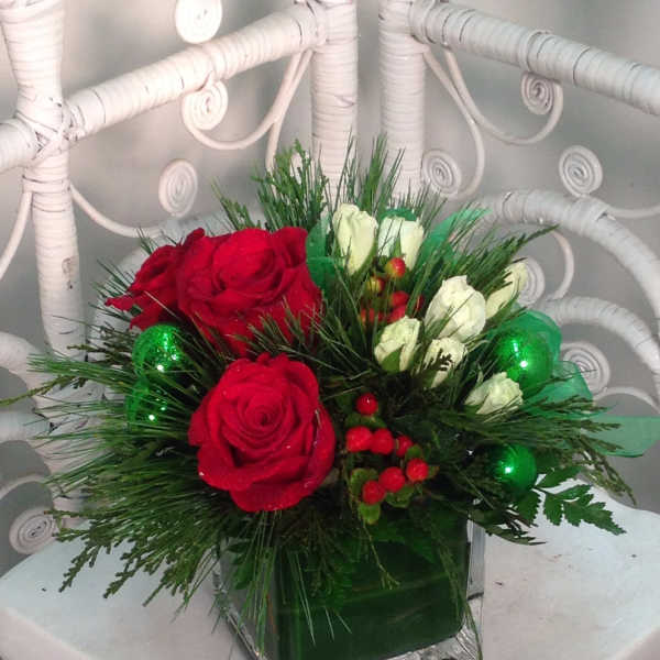 Red and white rose arrangement in a square glass vase with green accents