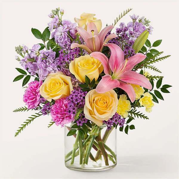 Bouquet of pink lilies, yellow roses, and purple flowers in a clear glass vase
