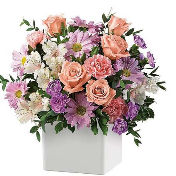 Mixed pink, purple, and white flowers in a white square vase