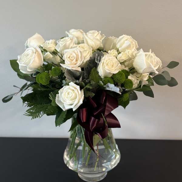 White rose bouquet in a clear glass vase with a burgundy ribbon