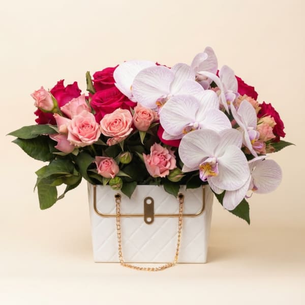 Pink roses and white orchids arranged in a white quilted handbag-style container