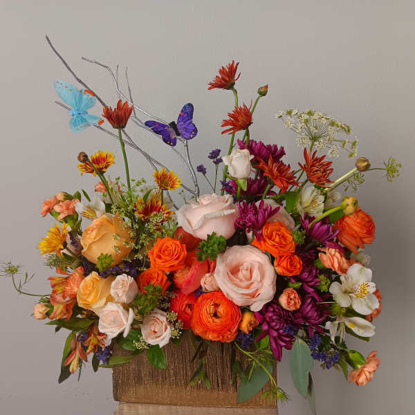 Colorful mixed flower arrangement in a gold vase with butterfly picks
