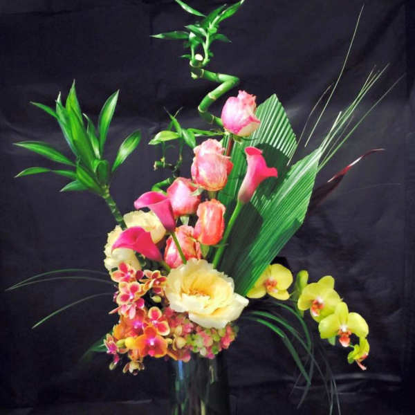 Tropical floral arrangement with pink and yellow orchids in a tall glass vase
