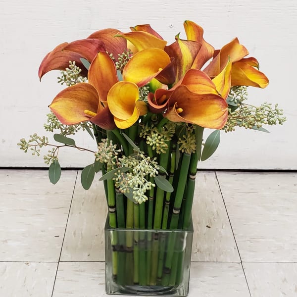 Orange and yellow calla lilies in a square glass vase