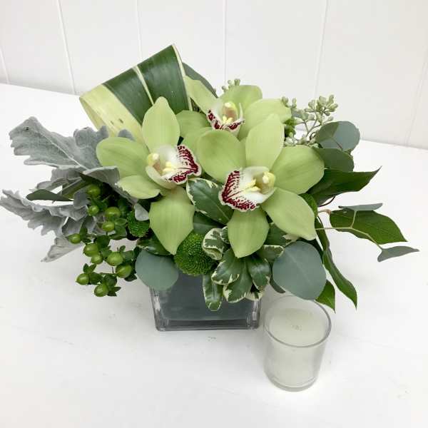 Green orchid arrangement in a square glass vase with a small candle