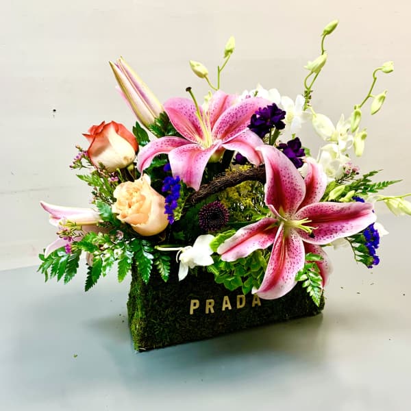 Pink lilies and roses arranged in a moss-covered Prada box