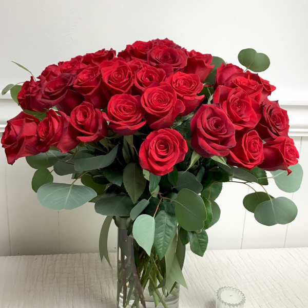 Bouquet of red roses in a clear glass vase with eucalyptus