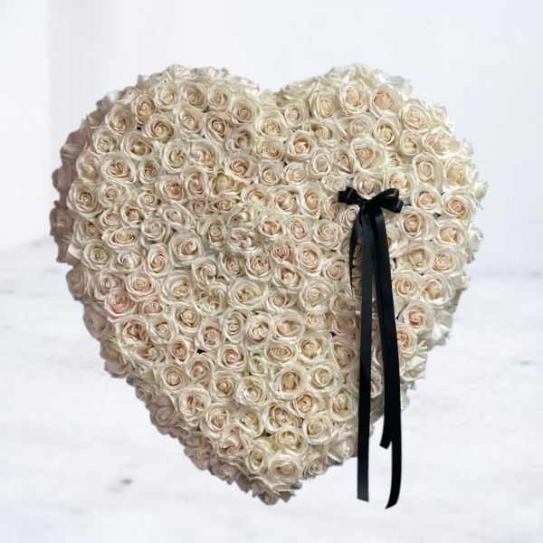 Heart-shaped arrangement of cream roses with a black ribbon bow on one side